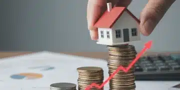 Hand placing a model house on coins, symbolizing the impact of rising interest rates on homeownership and mortgages.